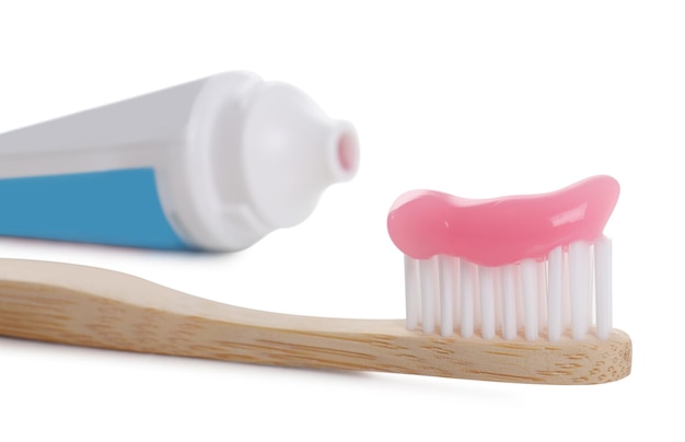 Cepillo de madera con pasta de dientes y tubo sobre fondo blanco primer plano