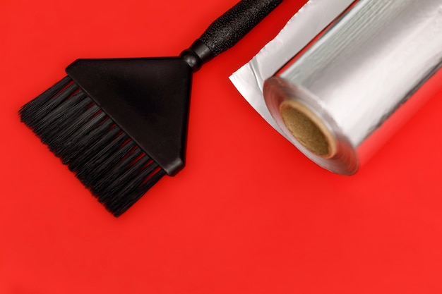Cepillo negro y rollo de papel de aluminio para teñir el cabello. Fondo rojo.