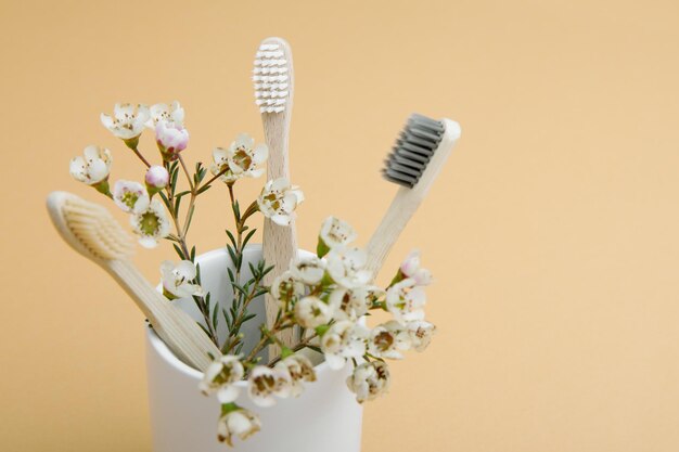 Cepillos de dientes de bambú de madera y flores en un vaso blanco sobre fondo beige El concepto de sostenibilidad y el rechazo del plástico El concepto de higiene y rutina diaria