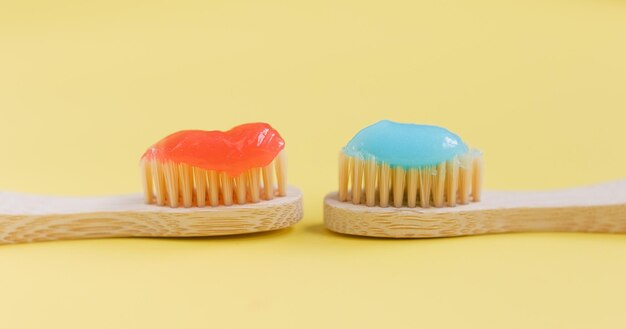 Cepillos de dientes de bambú de madera con pasta de dientes roja y azul sobre un fondo amarillo con espacio de copia Cero desperdicio Libre de plástico Concepto de estilo de vida sostenible Concepto de cuidado dental