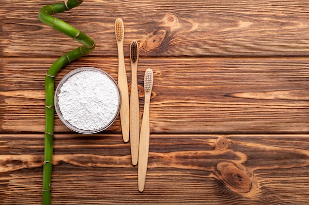 Cepillos de dientes de bambú, planta de bambú, polvo de dentífrico sobre fondo de madera. Espacio de copia laico plano. Cepillo de dientes de bambú natural biodegradable. Respetuoso del medio ambiente, Cero desperdicio, Cuidado dental Concepto sin plástico