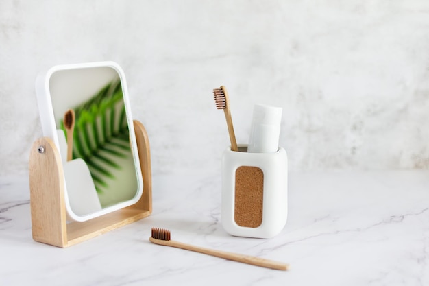 Cepillos de dientes de bambú en una taza de pasta de dientes y espejo sobre una mesa de mármol blanco en un baño Concepto de higiene dental de estilo de vida sostenible