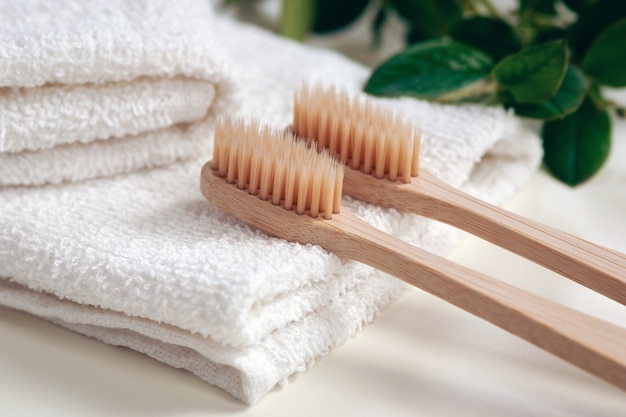 Cepillos de dientes de bambú, toallas y hojas de plantas verdes en un baño