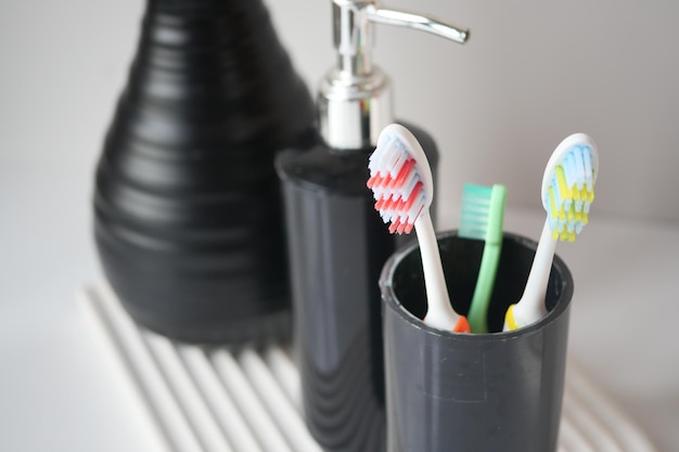 Cepillos de dientes de colores en taza blanca contra una pared.