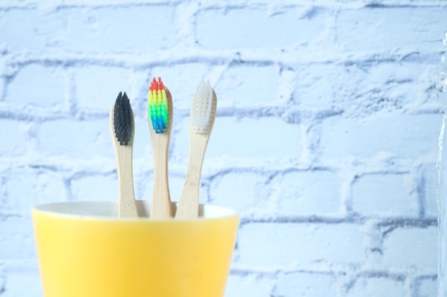 Cepillos de dientes de colores en taza blanca contra una pared.