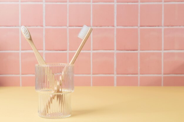 Cepillos de dientes ecológicos de bambú natural en un vaso sobre una mesa dentro de un baño, azulejos de pared, fondo de cerámica, espacio de copia