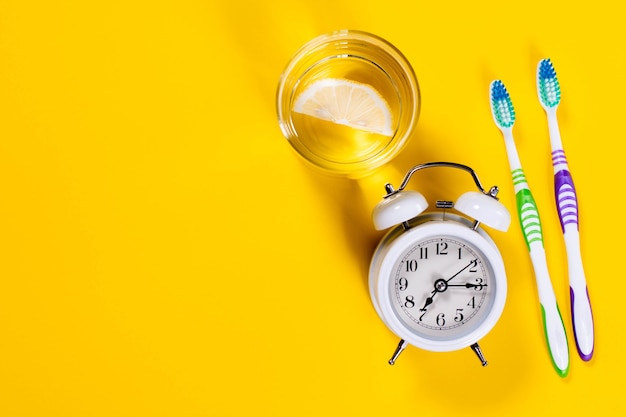 Cepillos de dientes, vaso de agua con limón y despertador