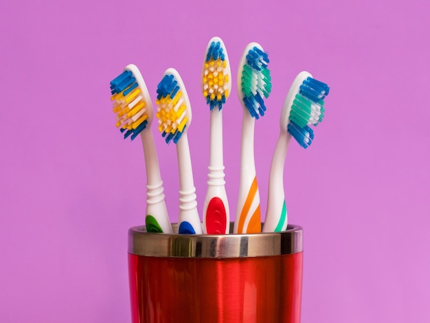 Cepillos de dientes en un vaso rojo sobre un fondo violeta. Cuidado dental