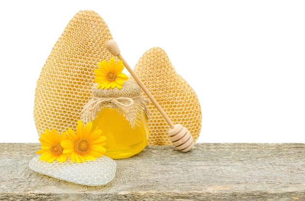 Cera de abejas con miel y flores sobre una tabla de madera sobre un fondo blanco.