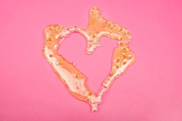 Foto cera de cannabis, extracto de marihuana shatter dab en forma de corazón dorado sobre fondo rosa.