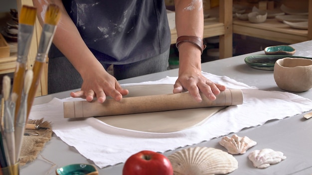 El ceramista que usa un rodillo rueda la arcilla para crear una placa de cerámica