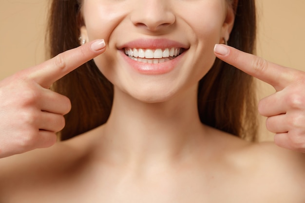 Cerca de 20 años mujer morena medio desnuda con una piel perfecta, maquillaje desnudo aislado en la pared de color beige pastel, retrato. Concepto de procedimientos cosméticos sanitarios para el cuidado de la piel.