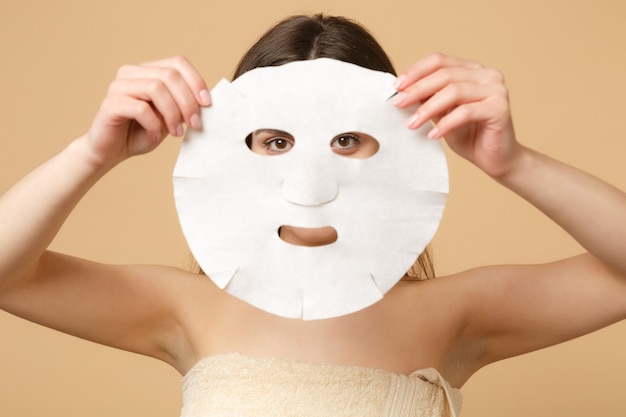 Cerca de 20 años mujer morena medio desnuda con una piel perfecta, maquillaje desnudo aislado en la pared de color beige pastel, retrato. Concepto de procedimientos cosméticos sanitarios para el cuidado de la piel.