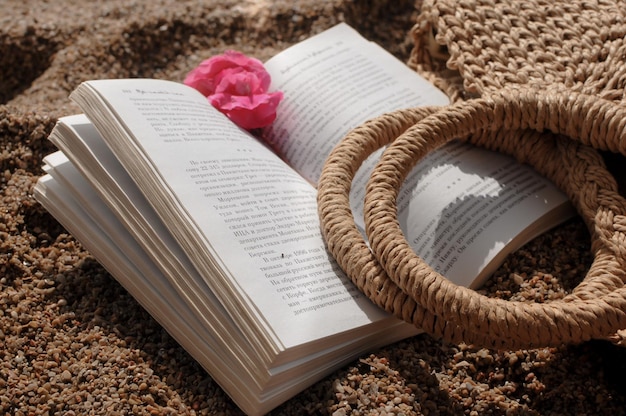 Foto cerca de accesorios de playa bolsa de punto de paja y un libro en una playa de arena