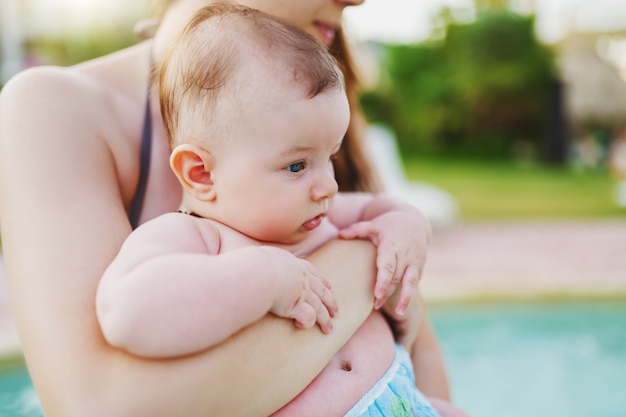 Cerca de adorable bebé de 6 meses de edad caucásica tener su primera vez en la piscina. Madre sosteniendo su apretado.