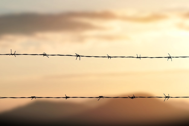 Cerca de alambre de púas con cielo crepuscular para sentirse silencioso y solo y querer libertad