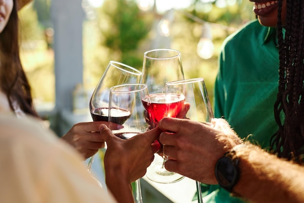 Cerca de amigos brindando con copas de vino en celebración durante la fiesta al aire libre en verano