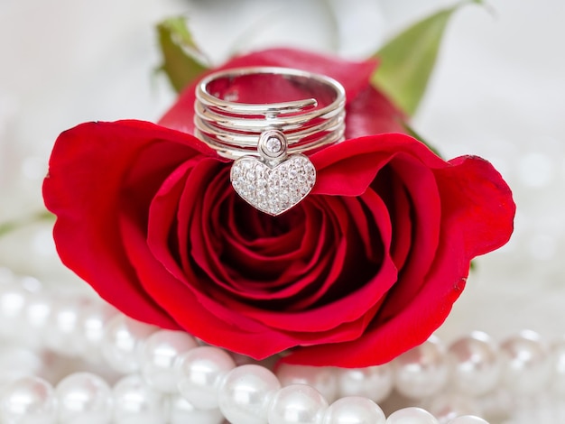 Cerca del anillo de diamantes en forma de corazón en la rosa roja y decorado con perlas alrededor