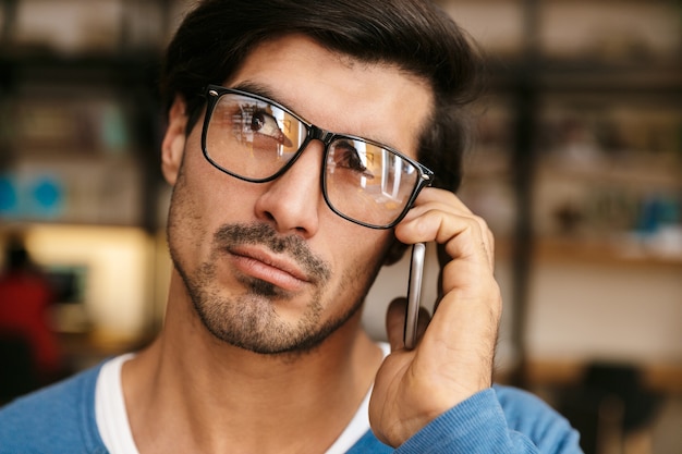 Cerca de un apuesto joven con gafas en la biblioteca, hablando por teléfono móvil