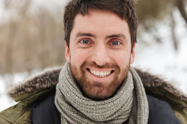 Cerca de un apuesto joven sonriente vistiendo chaqueta de invierno caminando al aire libre