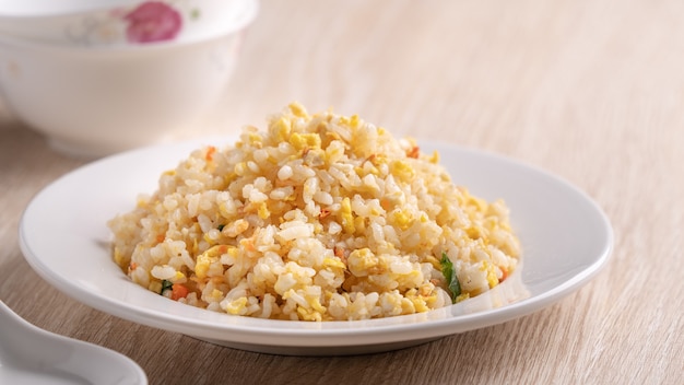 Cerca de arroz frito chino con camarones Sakura sergestid en plato blanco sobre fondo de mesa de madera brillante.