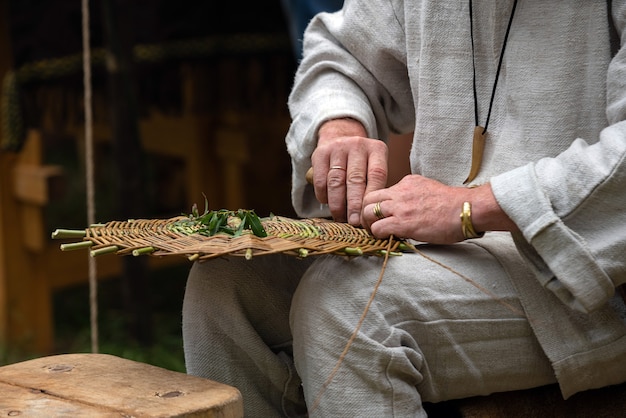 Cerca de artesano vistiendo ropa rural haciendo canasta de mimbre de ramitas.