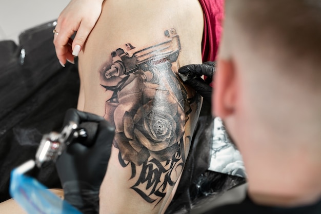 Cerca del artista masculino del tatuaje barbudo hace un tatuaje en una pierna femenina