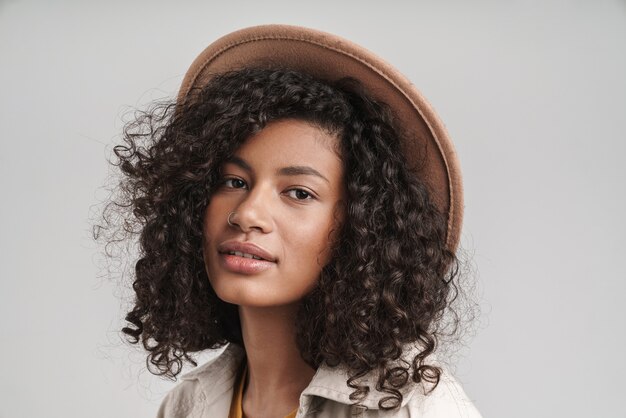 Cerca de una atractiva joven mujer africana sonriente con el pelo rizado, vistiendo abrigo de otoño y un sombrero