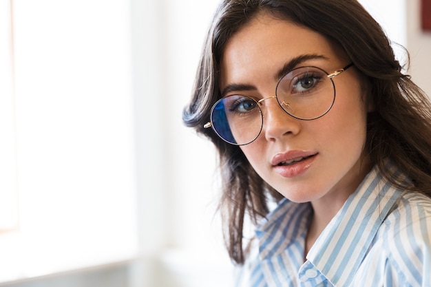 Cerca de una atractiva mujer morena con gafas y camisa en el interior