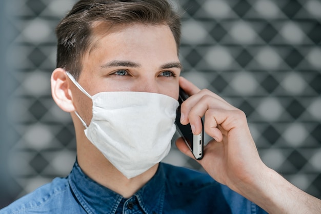 De cerca. atractivo joven con una máscara protectora hablando por un teléfono inteligente. coronavirus en la ciudad