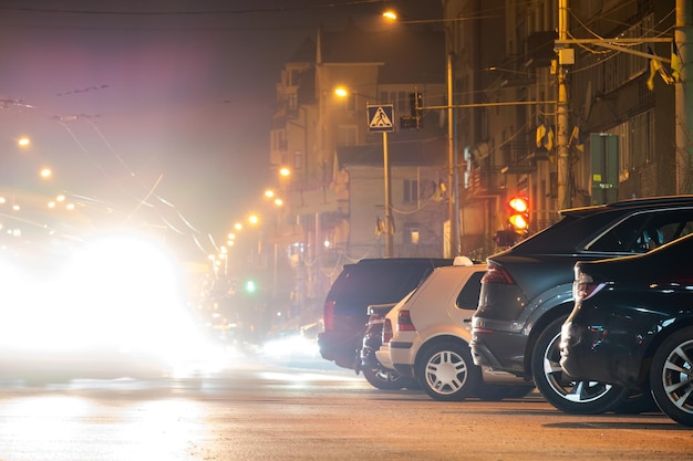 Cerca de los autos estacionados en la carretera por la noche con una vista borrosa de los semáforos de los vehículos en movimiento en las calles de la ciudad