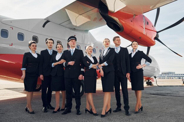 Foto cerca del avión tripulación de trabajadores del aeropuerto en ropa formal de pie juntos al aire libre