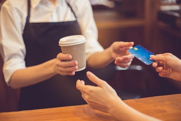 Cerca de barista profesional. Mujer dando taza de café y tomando tarjeta de crédito