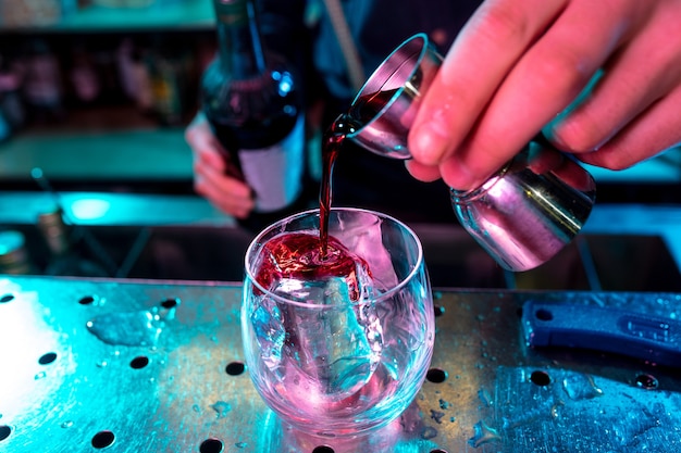 Cerca de barman preparación de cóctel alcohólico con tiro en luz de neón multicolor