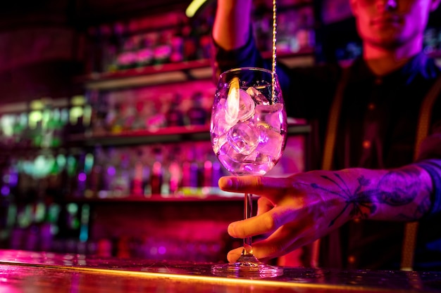 Foto cerca de barman profesional termina la preparación de cóctel alcohólico en luz de neón multicolor, se lo da al cliente. entretenimiento, bebidas, concepto de servicio. bar moderno, colores neón de moda.