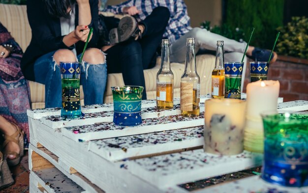 Cerca de bebidas sobre mesa de palets con confeti en una fiesta al aire libre con gente hablando en el fondo