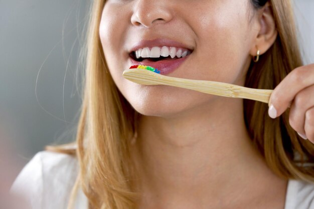 Cerca de la boca de la niña con cepillo de dientes de bambú ecológico Mujer feliz cepillarse los dientes con cepillo de dientes de bambú de madera