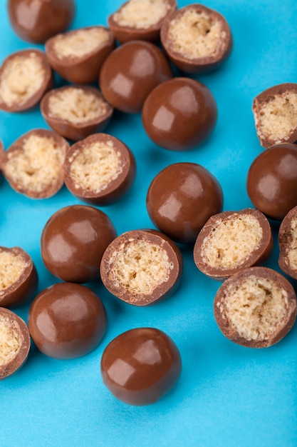 Cerca de bolas de caramelo de chocolate y mitades con relleno de maíz crujiente sobre fondo azul.