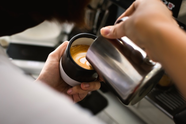 Cerca de café barista manos están haciendo arte latte.