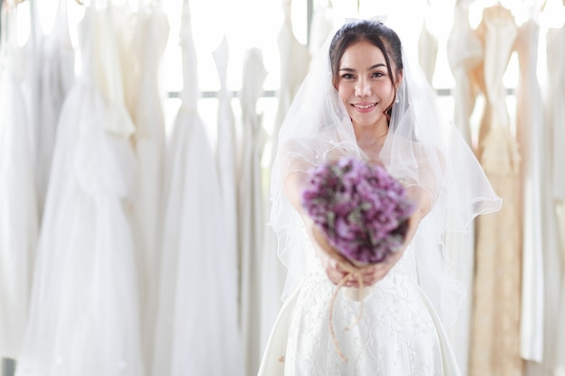 Cerca de la cara de la sonrisa La novia con un vestido de encaje blanco mano sosteniendo un ramo de flores púrpuras hacia adelante. Concepto feliz amor encantador casarse mejor día.