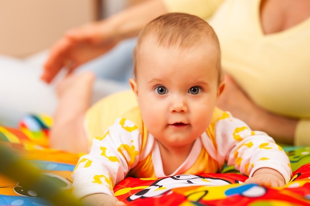 Cerca de la cariñosa hermosa joven madre enseña colores a su encantadora hija de seis meses acostada en una acogedora habitación para niños