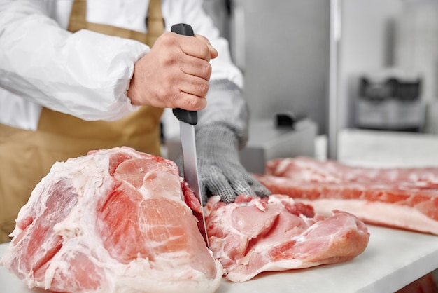 Foto cerca de carne cruda y carnicero cortar carne con cuchillo.