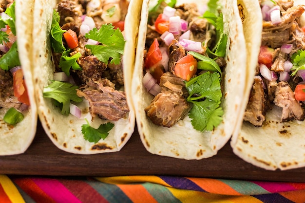 Cerca de carnitas de cerdo desmenuzado con pico de gallo sobre una tortilla de harina.