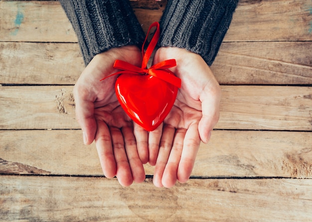 Cerca de la celebración de mano mujer y persona corazón rojo en la mesa de madera. Fondo de San Valentín.