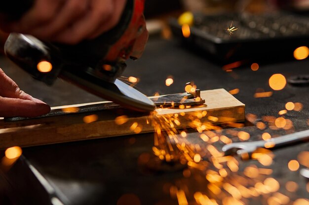 Foto de cerca el cerrajero trabaja con la máquina de moler volar chispas brillantes un hombre moliendo a mano un metal en el taller chispas en la metalurgia