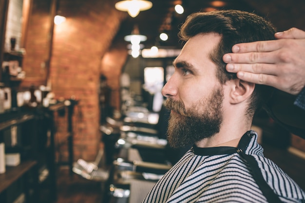 Foto cerca de un chico barbudo. su peluquero está cortando y modelando su cabello.