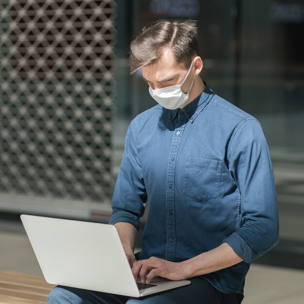 Foto de cerca. chico de ciudad con una máscara protectora está trabajando en una computadora portátil. concepto de protección de la salud.