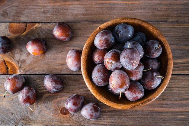 Cerca de ciruelas azules maduras en un recipiente de madera