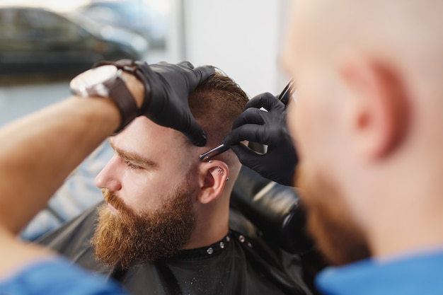 Cerca del cliente de servicio de peluquería profesional masculina, afeitado de barba grande y gruesa con navaja recta