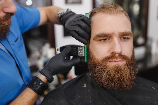 Cerca del cliente de servicio de peluquería profesional masculino con barba grande y gruesa por clipper